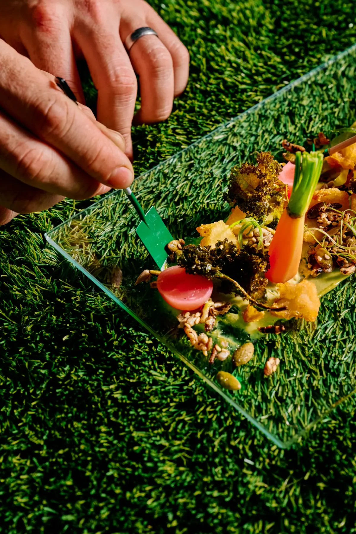 A chef placing a tiny flag with tweezers on a garden course laid over grass